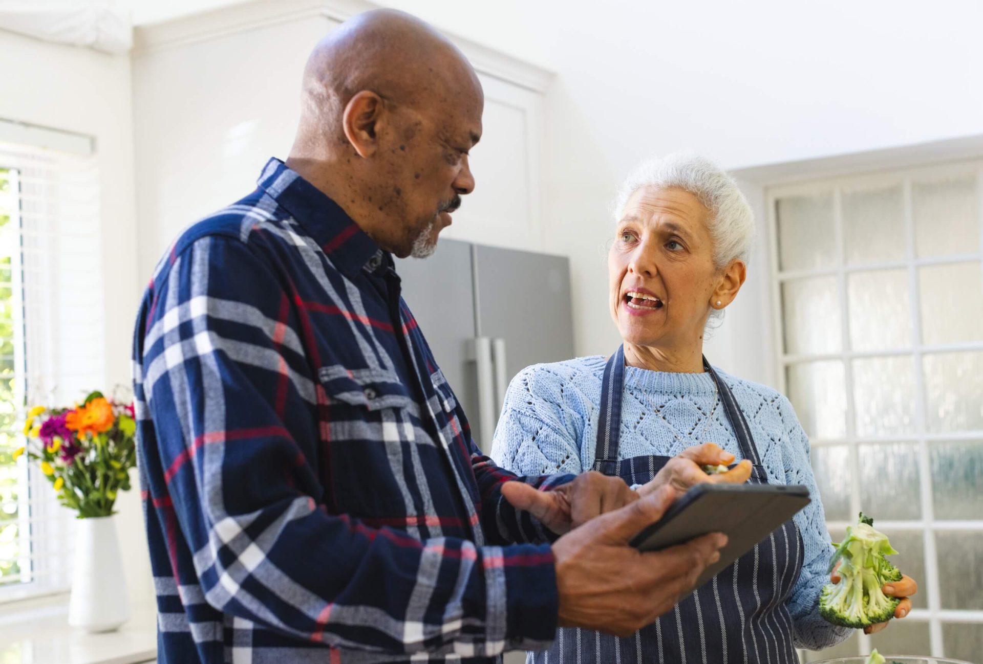Couple in kitchen holding a tablet, discussing a recipe.